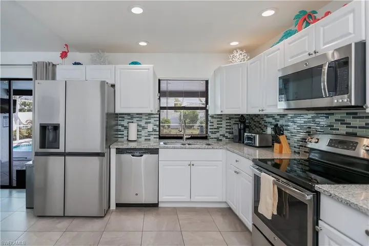 Kitchen featuring stainless steel appliances, light stone countertops, white cabinetry, decorative backsplash, and recessed lighting