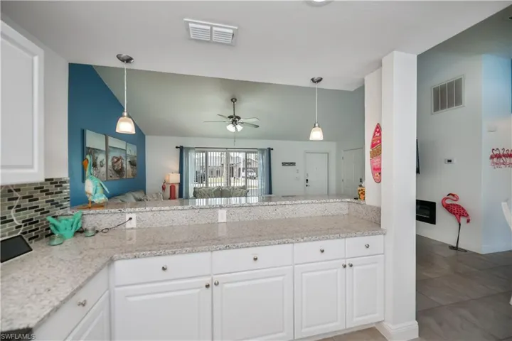 Kitchen with light stone counters, pendant lighting, vaulted ceiling, white cabinetry, and tasteful backsplash