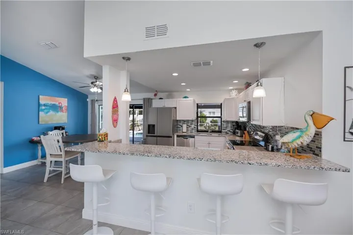 Kitchen with white cabinets, light stone countertops, stainless steel appliances, a breakfast bar area, and backsplash