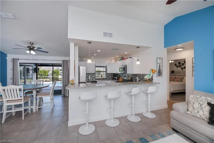 Kitchen with ceiling fan, a breakfast bar area, light stone countertops, and white cabinets