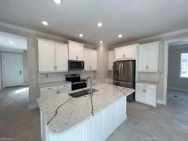 Kitchen with white cabinets, stainless steel appliances, light stone counters, a kitchen island with sink, and crown molding