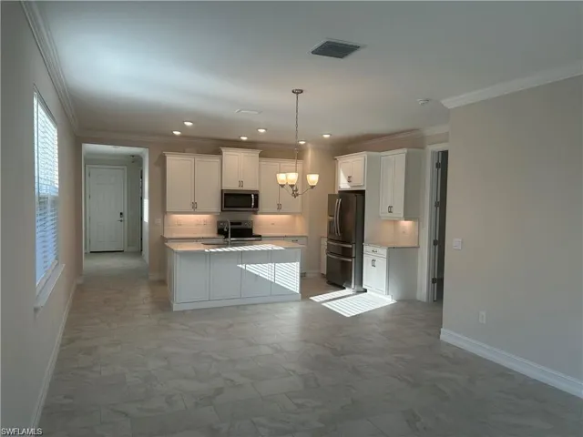 Kitchen with light countertops, white cabinetry, crown molding, stainless steel appliances, and an island with sink