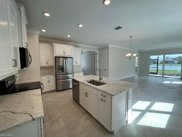 Kitchen featuring ornamental molding, stainless steel appliances, light stone counters, an island with sink, and white cabinetry