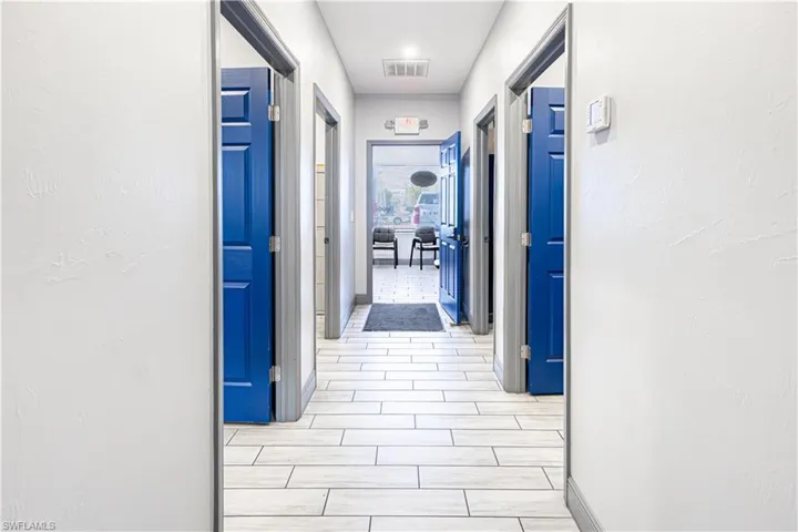 Hallway featuring wood-finish tile flooring, white walls, and paneled doors with blue accents
