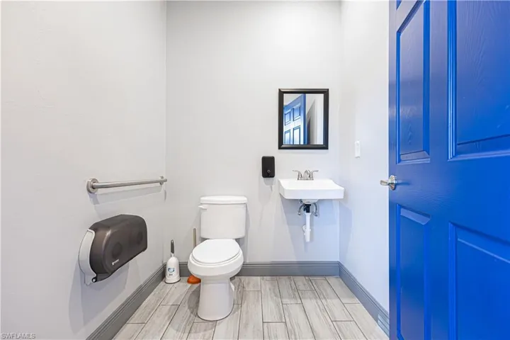 Wall-mounted sink with chrome faucet, a framed mirror, and wood-finish flooring