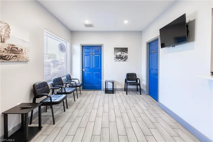 Wood-finish plank flooring, bright overhead recessed lighting, and a large window with horizontal blinds
