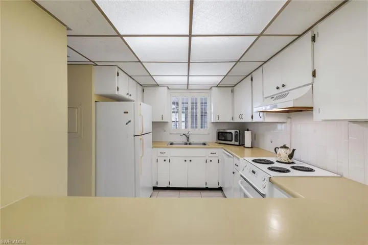 Kitchen with a paneled ceiling, sink, light tile patterned floors, white cabinetry, and white appliances