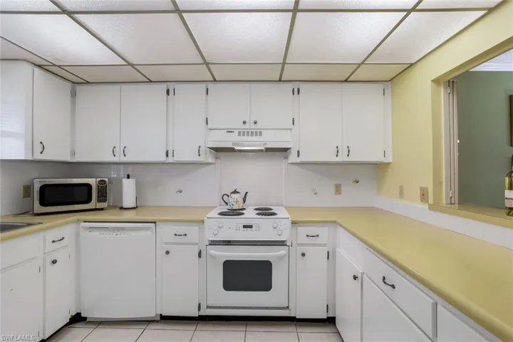 Kitchen featuring white appliances, white cabinetry, light tile patterned floors, and backsplash