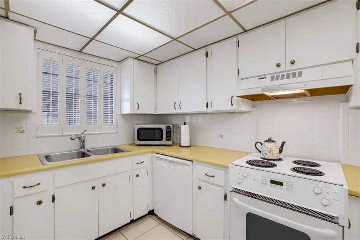 Kitchen featuring light tile patterned flooring, a paneled ceiling, sink, white cabinets, and white appliances