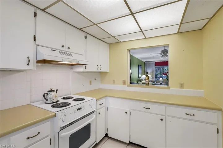 Kitchen featuring white electric range oven, decorative backsplash, a paneled ceiling, and white cabinetry