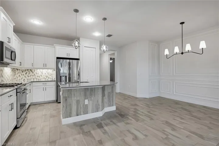 Kitchen featuring stainless steel appliances, white cabinets, a center island with sink, a decorative wall, and decorative backsplash