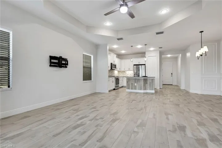 Unfurnished living room with a tray ceiling, a ceiling fan, wood tiled floors, and hanging lights