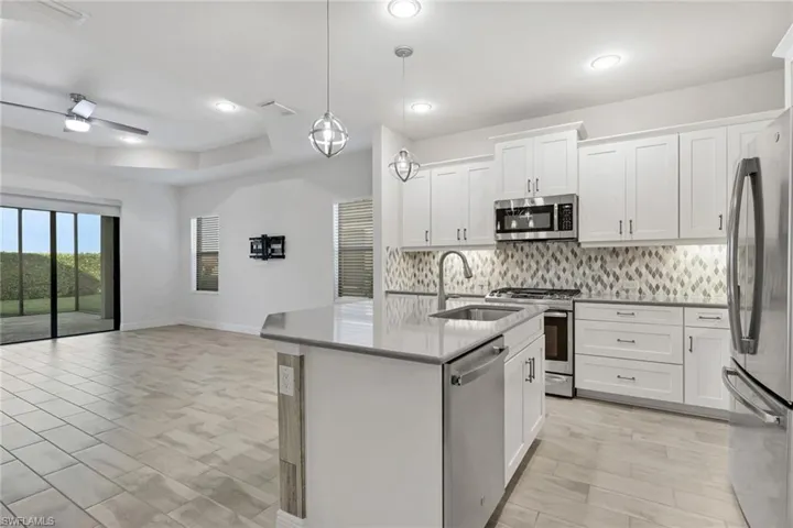 Kitchen with white cabinetry, stainless steel appliances, a center island with sink, open floor plan, and light stone countertops