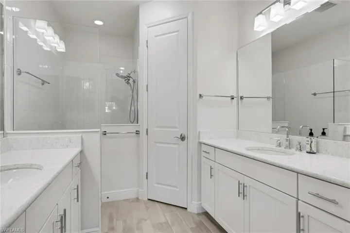 Bathroom featuring two vanities, a walk in shower, and light wood finished floors