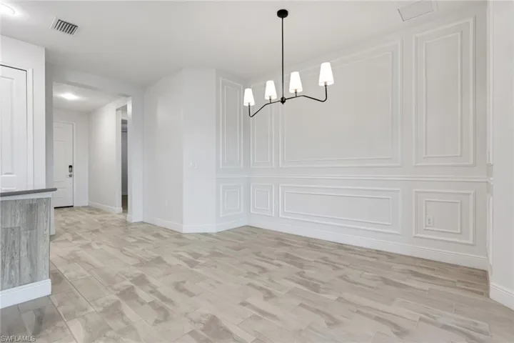 Unfurnished dining area with a chandelier, light wood-style floors, and a decorative wall