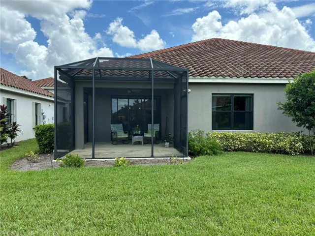 Back of house featuring a yard, a sunroom, a lanai, stucco siding, and a tiled roof