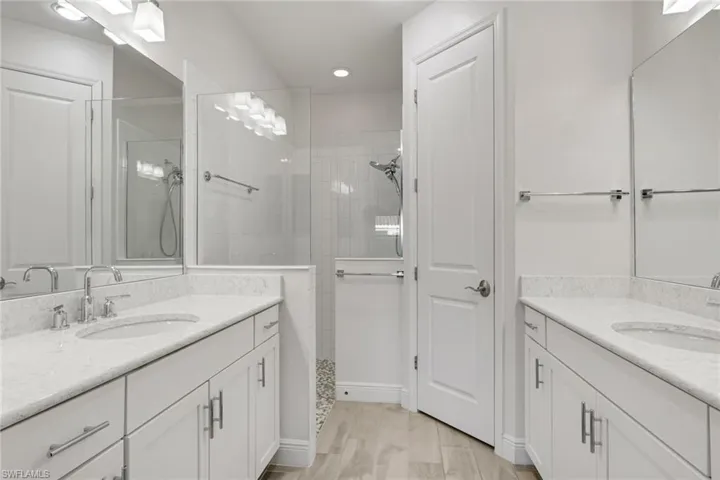 Full bath with two vanities, a walk in shower, light wood-style floors, and a closet