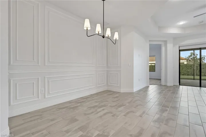 Unfurnished dining area with a decorative wall, a chandelier, a raised ceiling, and light wood-style floors