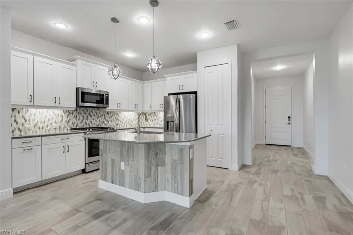 Kitchen with stainless steel appliances, white cabinets, a kitchen island with sink, light wood-style flooring, and dark stone countertops