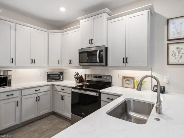 Kitchen with a sink, appliances with stainless steel finishes, recessed lighting, light stone countertops, and backsplash