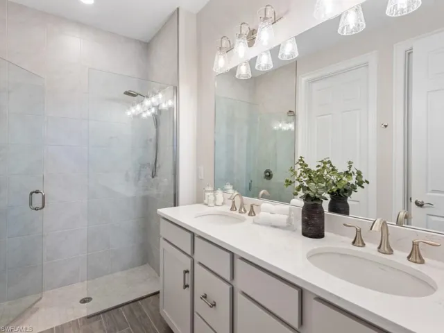 Full bath featuring double vanity, a sink, a stall shower, and wood finished floors