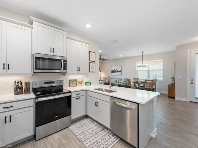 Kitchen featuring a peninsula, appliances with stainless steel finishes, light countertops, a sink, and light wood finished floors
