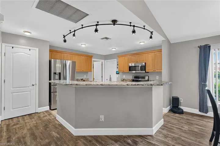 Kitchen featuring a multi-level island with a light-colored countertop, wood-finish flooring, recessed ceiling lighting, light wood cabinetry, and stainless steel appliances