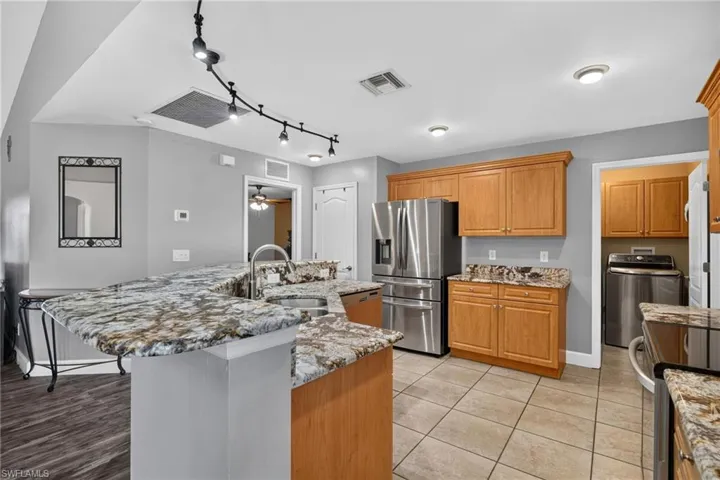 Kitchen featuring light wood cabinetry, stone countertops, stainless steel refrigerator, tile flooring, and track lighting