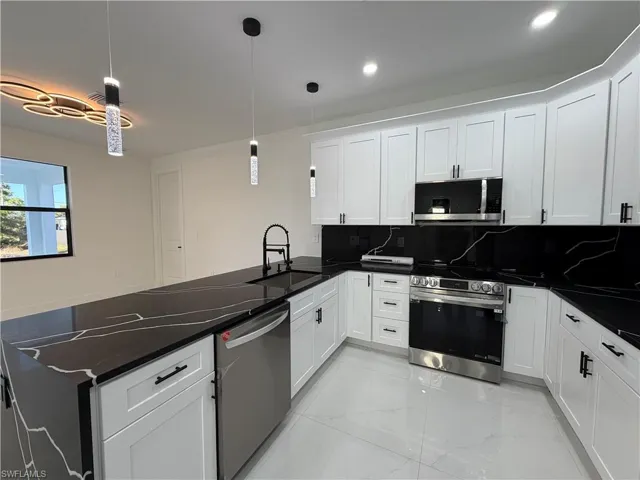 Kitchen with stainless steel appliances, white cabinetry, light marble finish flooring, backsplash, and dark stone countertops