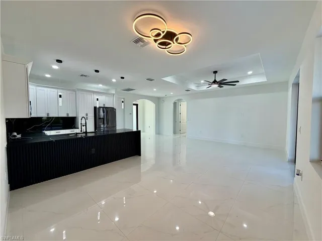 Kitchen with arched walkways, a peninsula, open floor plan, black refrigerator with ice dispenser, and a raised ceiling