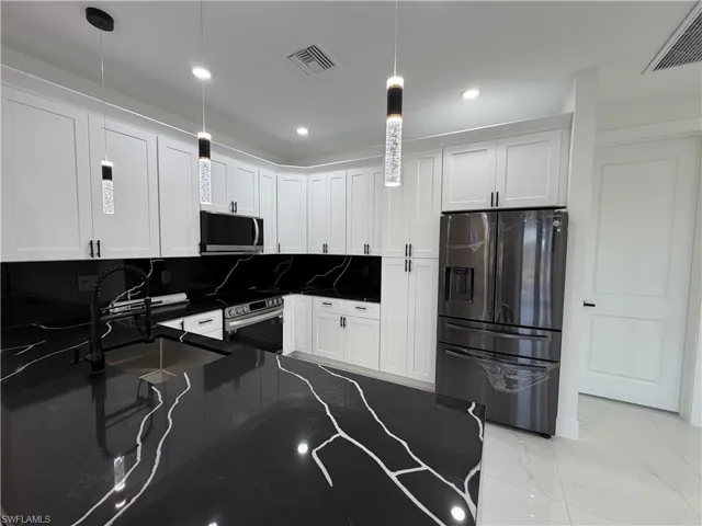 Kitchen with stainless steel appliances, white cabinets, dark stone counters, light marble finish floors, and decorative backsplash