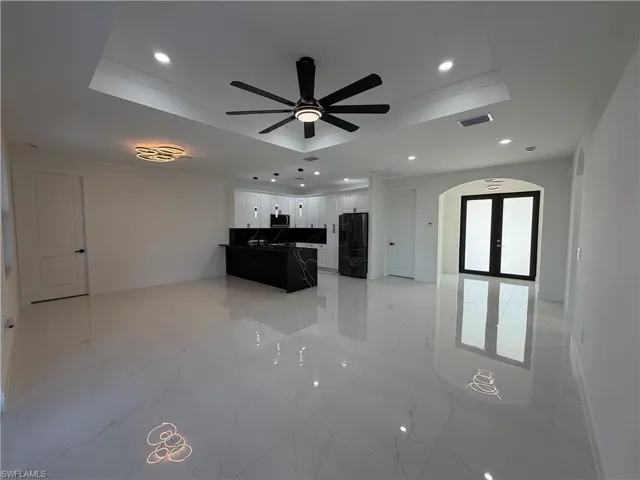 Unfurnished living room with ceiling fan, recessed lighting, light marble finish floors, a tray ceiling, and french doors