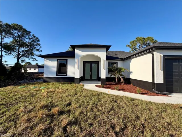 View of front of house featuring french doors, a garage, a front lawn, and stucco siding