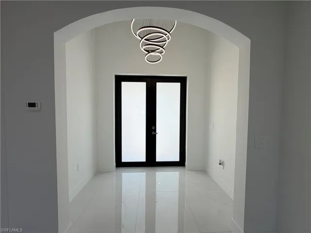 Entryway with arched walkways, french doors, light marble finish flooring, and hanging lights