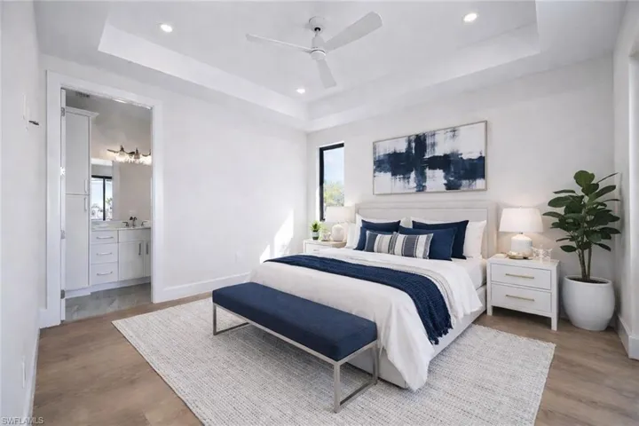Virtually Staged. Bedroom featuring light wood-style flooring, multiple windows, recessed lighting, a tray ceiling, and connected bathroom