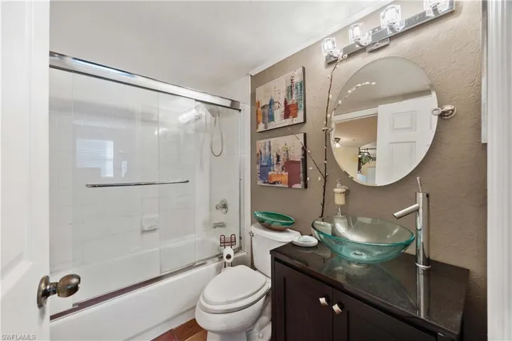 Full bathroom featuring vanity, enclosed tub / shower combo, toilet, and a textured ceiling