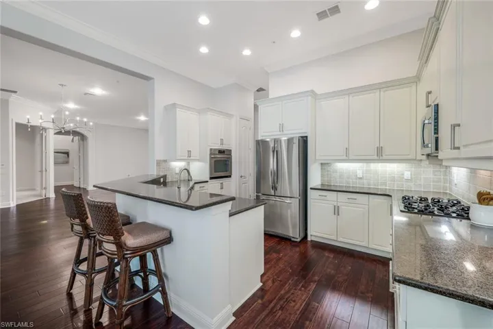 Kitchen with backsplash, kitchen peninsula, dark wood-type flooring, and stainless steel appliances