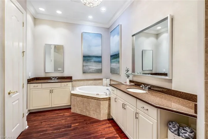Bathroom with crown molding, tiled bath, double vanity, and hardwood / wood-style floors