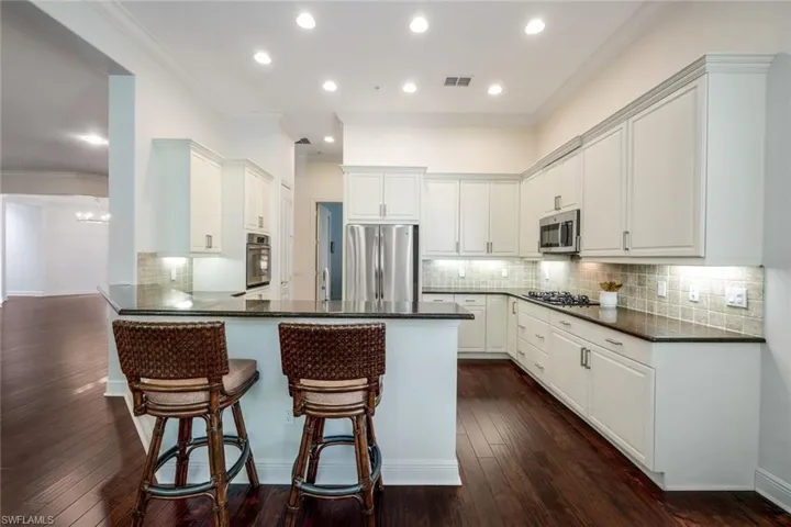 Kitchen with ornamental molding, dark wood-type flooring, backsplash, and appliances with stainless steel finishes