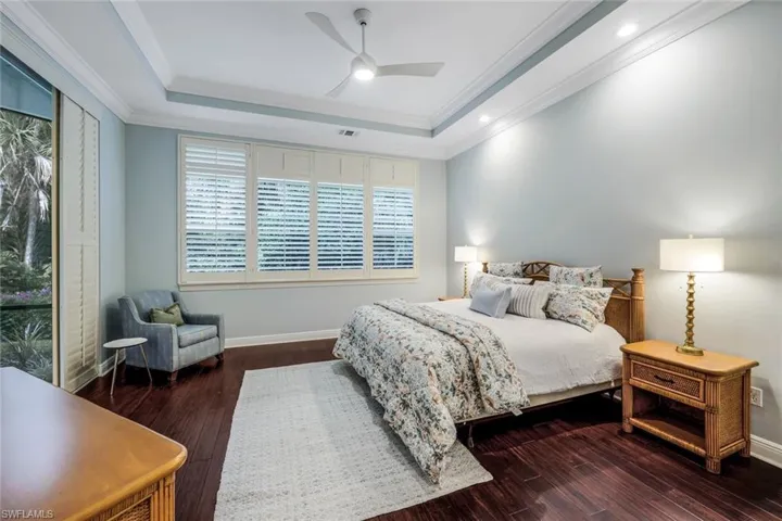 Bedroom with ornamental molding, ceiling fan, a raised ceiling, and dark hardwood / wood-style floors