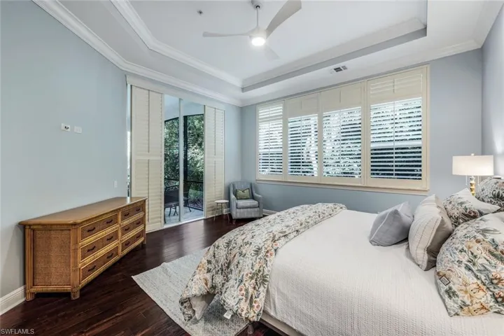 Bedroom with ceiling fan, multiple windows, a tray ceiling, and dark hardwood / wood-style flooring