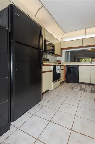 Two tone kitchen with black appliances, light countertops, light tile patterned floors, and two tone cabinetry