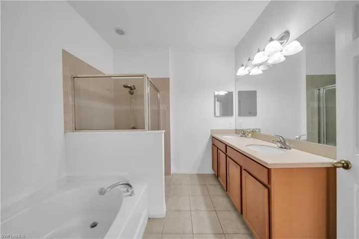 Full bathroom with a garden tub, double vanity, light tile patterned floors, and a shower stall