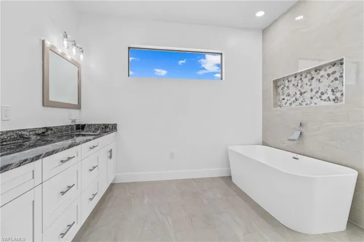 Full bathroom featuring vanity, a freestanding tub, tile walls, and recessed lighting