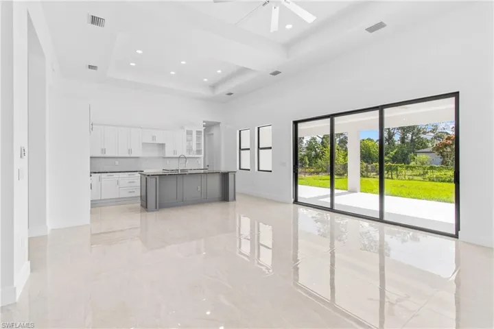 Kitchen featuring open floor plan, an island with sink, glass fronted cabinets, a tray ceiling, and recessed lighting