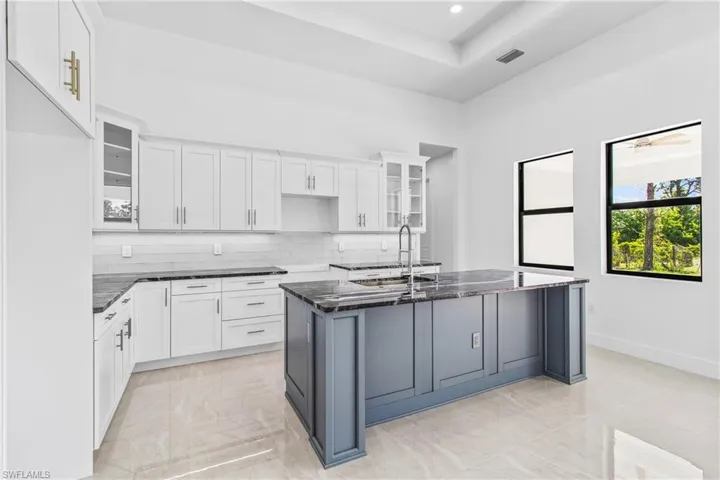 Kitchen with glass fronted cabinets, dark stone countertops, an island with sink, decorative backsplash, and two tone cabinetry