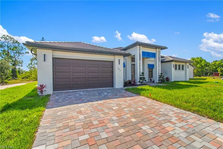 Prairie-style house featuring a front yard, decorative driveway, stucco siding, and an attached garage