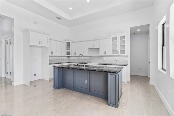 Two tone kitchen with glass insert cabinets, a center island with sink, dark stone countertops, recessed lighting, and two tone cabinets