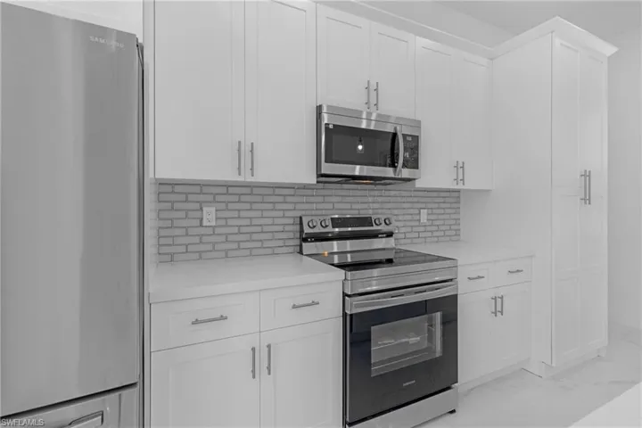 Kitchen with stainless steel appliances, white cabinetry, light tile flooring, and tasteful backsplash