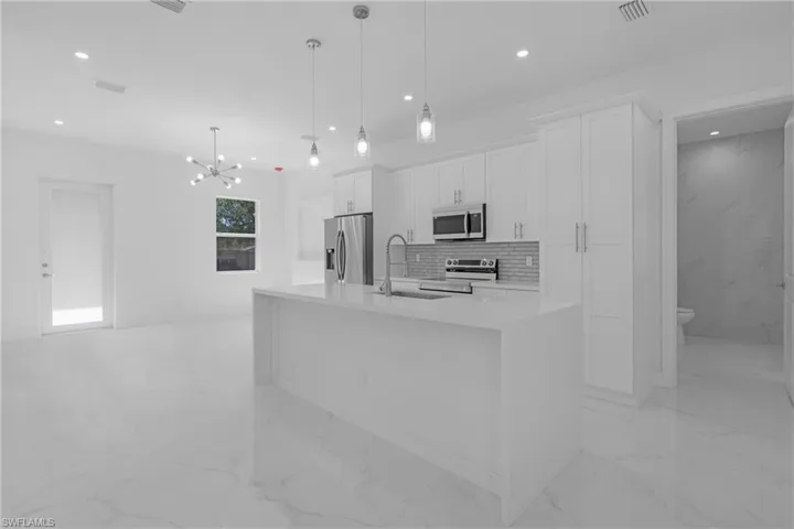 Kitchen featuring light tile floors, a kitchen island with sink, white cabinetry, and appliances with stainless steel finishes